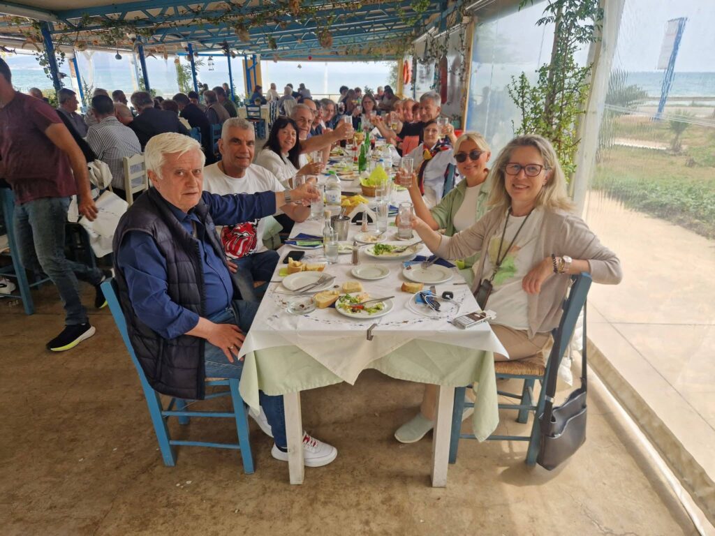 Η μονοήμερη εκδρομή της Ε.ΣΥΝ.Α.Α. στο Ναύπλιο που άφησε εποχή. Ποιος είπε ότι η σύνταξη είναι σιωπή και ρουτίνα; Όποιος τολμούσε να το σκεφτεί, ας βρισκόταν εκείνη την κυριακάτικη της 10ης Μαΐου 2026, στην αφετηρία της Ένωσης Συνταξιούχων Αστυνομικών Αττικής. Αντί για γκρίζα ξύπνια, επικρατούσε αναστάτωση… από χαμόγελα. Τα πούλμαν γέμισαν ασφυκτικά από μέλη, φίλους, ζευγάρια, παλιούς συναδέλφους που δεν είχαν συναντηθεί από την εποχή των περιπολιών. Ο Ισθμός ως πρελούδιο: ένα τσιγάρο, ένας καφές και μια αγκαλιά Όπως αρμόζει σε κάθε σωστή περιοδεία, η πρώτη στάση έγινε στον Ισθμό της Κορίνθου. Όχι για να δουν απλώς τη διώρυγα – την έχουν δει χίλιες φορές. Εδώ, το νόημα ήταν άλλο. Παλιοί συνάδελφοι αντάλλαξαν χειραψίες που κράτησαν λίγο παραπάνω. «Ρε σύ, θυμάσαι εκείνη την υπόθεση;», ακούστηκε κάπου, ακολουθούμενο από ένα ξέσπασμα γέλιου. Η πρώτη πρωτεύουσα υποκλίνεται στους ένδοξους "απόμαχους" Λίγο αργότερα, μπροστά στα μάτια τους ξεδιπλώθηκε το Ναύπλιο. Όχι το Ναύπλιο του τουρίστα, αλλά εκείνο του μύθου: γαλήνιο, αγέρωχο, με το Μπούρτζι να έχει βγει για ψάρεμα μέσα στο γαλάζιο, και το Παλαμήδι να αγναντεύει τις κινήσεις τους από ψηλά – ακριβώς όπως κι εκείνοι κάποτε αγνάντευαν τις γειτονιές της Αθήνας. Η περιήγηση άρχισε στην Πλατεία Συντάγματος. Εκεί, όπου ο Τρικούπης οραματίστηκε το μέλλον, εκείνη τη στιγμή οι συνταξιούχοι έγραφαν το δικό τους παρόν: χωρίς βία, χωρίς συναγερμούς, μόνο με το θρόισμα των πεταλούδων από τα αρχοντικά της Ενετοκρατίας. Κάποιος συνάδελφος, παλαίμαχος της Άμεσης Δράσης, σχολίασε μεταξύ σοβαρού και αστείου: «Εδώ, ακόμα και οι μπουκαμβίλιες στέκονται προσοχή». Γεύμα δίπλα στο κύμα: Η έκπληξη "Μαϊστράλι" Η έκπληξη όμως ήταν κρυμμένη λίγα χιλιόμετρα παρακάτω, στον Νέα Κίο. Το εστιατόριο «Μαϊστράλι» δεν ήταν απλά ένα μέρος για φαγητό – ήταν στάση καρδιάς. Ο ιδιοκτήτης και το προσωπικό, σαν να περίμεναν βασιλική αποστολή, είχαν στήσει ένα μενού που δεν τολμάς να ονειρευτείς ούτε σε γλέντι: φρέσκο ψάρι που μύριζε αλμύρα από το απέναντι κύμα, κρασί παγωμένο σαν τα πρώτα χιόνια του Ταΰγετου, και ορεκτικά που εξαφανίζονταν πιο γρήγορα κι από στοιχεία σε απόρρητη δικογραφία. Τα λόγια περισσεύουν. Αρκεί να πούμε πως στο τέλος, οι συνταξιούχοι συνάδελφοι ευχαρίστησαν τους ανθρώπους της κουζίνας. Ο "απρόσκλητος" επισκέπτης που έγινε ο πιο αγαπημένος Ανάμεσα στις εκπλήξεις, μια απρόσμενη. Όταν όλοι νόμιζαν ότι η μέρα τελείωσε, εμφανίστηκε στην παρέα ο Αντιδήμαρχος Καθαριότητας του Δήμου Άργους, κ. Χάρης Σελλής. Δεν ήταν όμως οποιοσδήποτε. Συνταξιούχος αστυνομικός ο ίδιος, πέρασε όλο το υπόλοιπο της εκδρομής μαζί τους – χωρίς καρέκλα τιμής, χωρίς λόγους. Κάθισε δίπλα στους παλιούς του συναδέλφους του, θυμήθηκε ονόματα και περιστατικά. «Εδώ, η σκούπα είναι εύκολη υπόθεση. Δύσκολο είναι να κρατάς τον συναδελφικό δεσμό αναμμένο ύστερα από τόσα χρόνια», είπε, συγκινημένος. Το "ευχαριστώ" που δε χωράει σε δελτίο τύπου Η Ε.ΣΥΝ.Α.Α., με την ευκαιρία αυτή, ευχαριστεί δημόσια: • Τον οδηγό του πούλμαν • Τον υπέροχο ανθρώπους της ταβέρνας «Μαϊστράλι» για την φιλοξενία που σε κάνει να ξεχνάς την πείνα με το γευστικό μενού της. Πάνω απ’ όλα όμως, ευχαριστεί τα μέλη της που συμμετείχαν στην εκδρομή. Το αύριο ξεκίνησε ήδη χθες Σήμερα, όλοι γύρισαν σπίτια τους με μια χούφτα αναμνήσεις: ένα βραχιολάκι από το Παλαμήδι, μια φωτογραφία στον Ισθμό, τον αριθμό τηλεφώνου από έναν χαμένο συνάδελφο που ξαναβρέθηκε. Κι επίσημα πια, το Διοικητικό Συμβούλιο της Ε.ΣΥΝ.Α.Α. να ανακοινώσει ότι επόμενες δράσεις βρίσκονται ήδη στο σχεδιασμό – και αν κρίνουμε από την απίστευτη συμμετοχή, η επόμενη θα έχι πολύ περισσότερες συμμετοχές. Μέχρι τότε, καλό καλοκαίρι. Και να το θυμάστε: η πατρίδα δεν είναι μονάχα εκεί που υπηρετήσατε. Είναι κι εκεί που γελάτε.